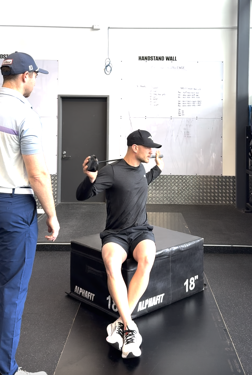 Coach watching a client perform a rotational cable exercise on a plyo box